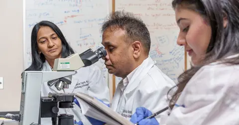 three scientists working in a lab wearing lab coats