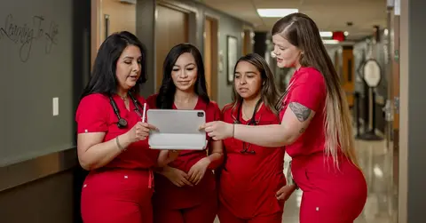 four nurses in red scrubs looking at an ipad