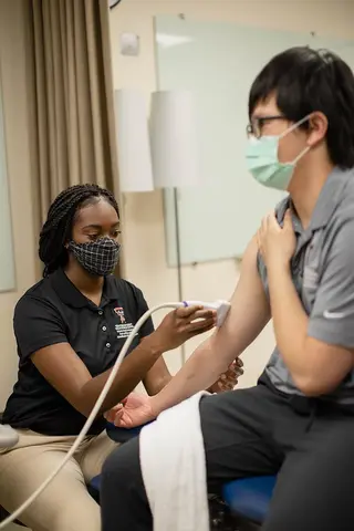 masked health care professional sitting with patient
