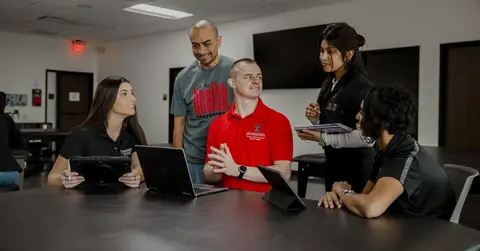 students talking and looking at their laptops at a conference table