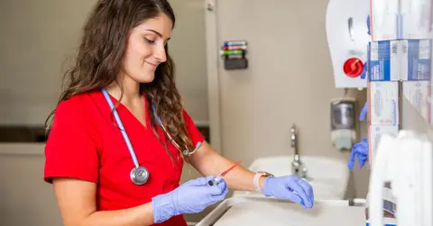 Nursing student wearing TTUHSC red scrubs and gloves.
