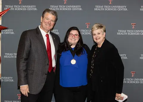  three people stand in front of a TTUHSC step and repeat