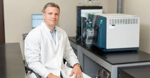 Male TTUHSC researcher wears a white coat and sits in his lab.