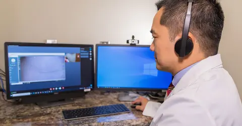 Male surgeon sits at a computer with headphones on.