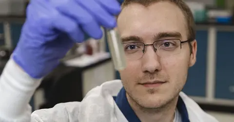 man in labcoat looking at vile