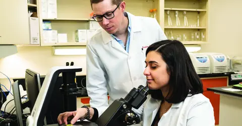 Schniers working in a lab at a microscope with a fellow student.