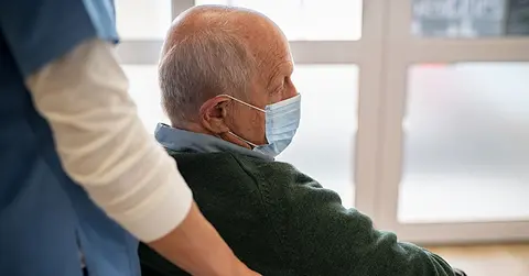 elderly man wearing mask with health care professional pushing him in a wheelchair