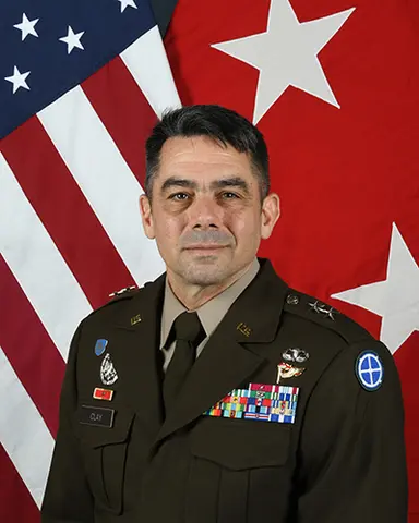 Man wears army uniform with U.S. flag behind him.
