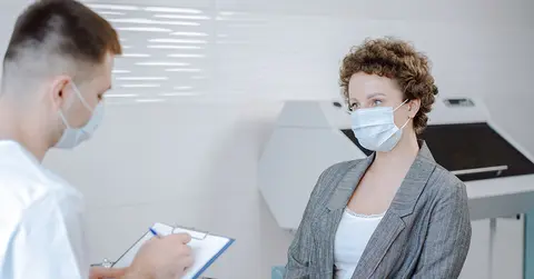 doctor looking at clipboard with patient, wearing masks