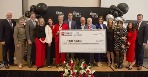 Large group of people stand on stage and hold a large presentation check.