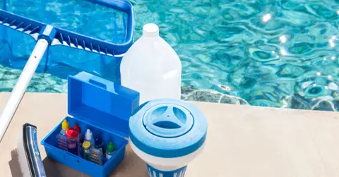 Pool chemicals and a net sit next to a swimming pool.