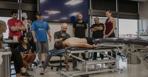 man in physical rehabilitation on a table with students and a professional around him 