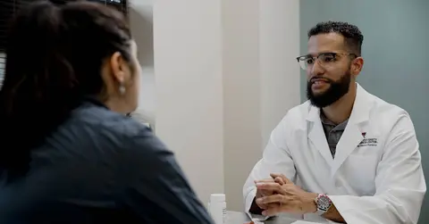 two people talking, one of whom is wearing a school of pharmacy white coat