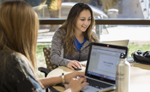 female students working at laptop in social setting